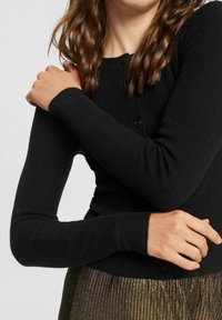 Zwarte geribde cardigan met lange mouwen en knoopsluiting, voorzien van een structuur gebreid patroon. Zacht materiaal met een aansluitend ontwerp.