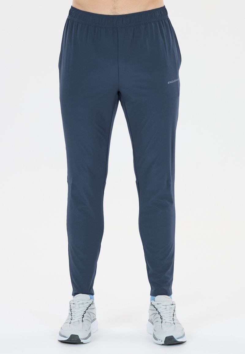 Mann trägt marineblaue, eng anliegende Sporthose mit elastischem Bund und weißen Laufschuhen, gezeigt von der Taille bis zu den Füßen.