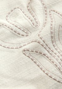 Tissu beige avec motifs de feuilles brodées en relief, délimités par un fil beige très serré, créant un design botanique texturé.