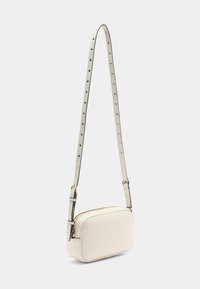 Valkoinen olkalaukku, jossa on sileä pinta, suorakulmainen muoto, kultaiset varusteet ja ohut, säädettävä hihna, jossa on reikäkoristeita.