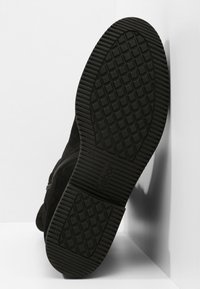 Černá semišová kotníková bota s texturovanou gumovou podrážkou s diamantovým vzorem, vybavená bočním zipem pro snadné obouvání.