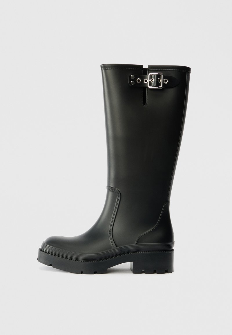 Botte de pluie en caoutchouc noir avec une texture lisse, hauteur mi-mollet, semelle épaisse et un détail de sangle à boucle pour une touche de design supplémentaire.