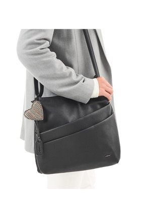 Person wearing gray coat holds black leather shoulder bag with textured surface and plaid heart-shaped keychain.
