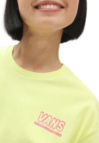 Camiseta de algodón verde lima con el logo rosa de "VANS" en el lado izquierdo del pecho, con cuello redondo y textura suave.