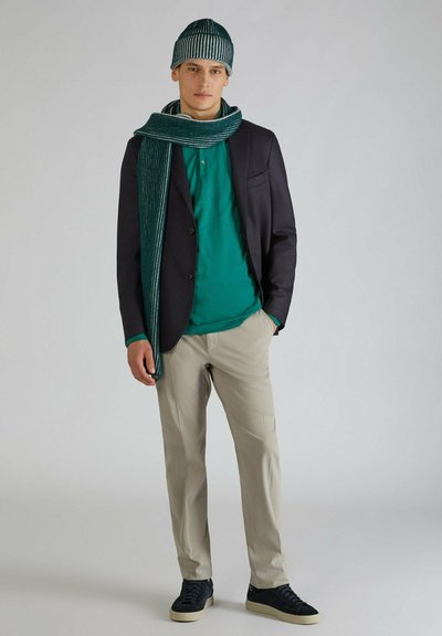 Outfit casual composto da un blazer blu navy sopra una maglietta verde acqua, pantaloni crema e sneakers blu navy. Accessoriato con una sciarpa a strisce verdi e un cappello.