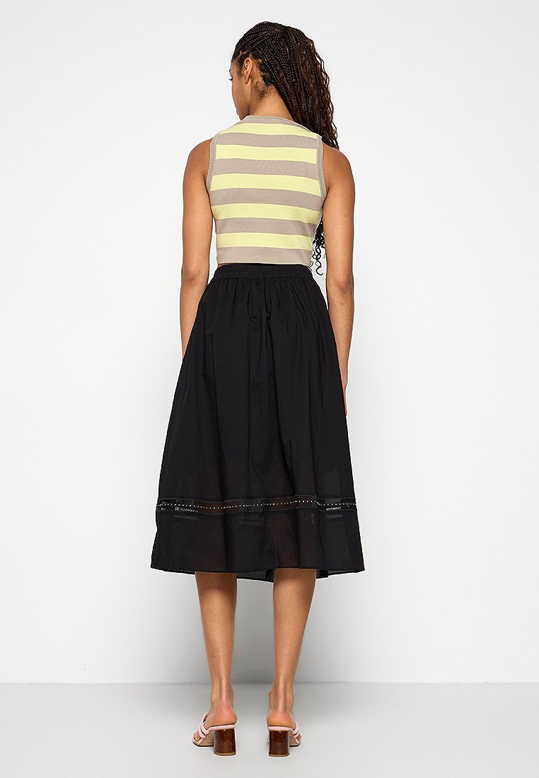 Bezrekawnikowy prążkowany top w szaro-żółte paski, zestawiony z czarną spódnicą do kolan z przezroczystym wykończeniem i dekoracyjnym przeszyciem.