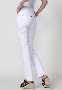 Baltas džinsi ar taisnu piegulmi, ar dekoratīvām izšuvēm sānos, kopā ar melnām sanāku sandalēm.