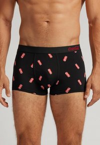 Svarta boxershorts med ett mönster av röda Coca-Cola-burkar. Tillverkade av elastiskt material med en svart midja som visar Coca-Cola-logotypen.
