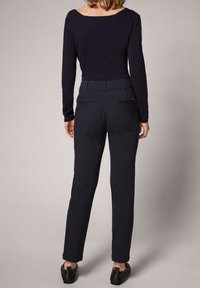 Haut noir à manches longues avec un large décolleté, associé à un pantalon noir tailleur. Le pantalon a une texture lisse et des poches arrière.