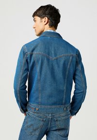 Mörkblå denimjacka med klassisk passform, synlig sömnad och spetsig krage. Har knappdetaljer och en något texturerad yta.