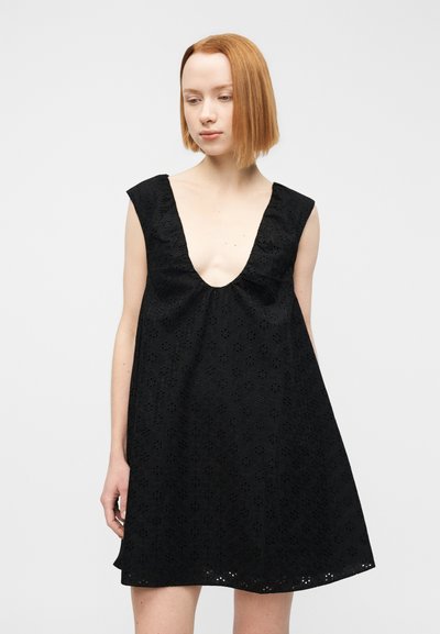 Μαύρο φόρεμα με βαθύ V λαιμόκοψη, κοντά μανίκια και υφάσμα με λουλουδάτη ανοιχτή ύφανση. Ο σχεδιασμός είναι φαρδύς, με φαρδιά γραμμή και υφή στην επιφάνεια.