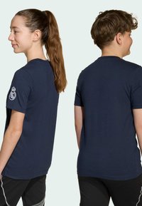 Námornícky modré tričko vyrobené z bavlny, s krátkymi rukávmi a okrúhlym výstrihom. Detaily zahŕňajú logo na ľavom rukáve.