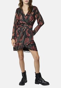 Robe noire avec un motif floral multicolore, décolleté en V, manches longues, taille cintrée, ourlet asymétrique, associée à des bottes de combat noires.