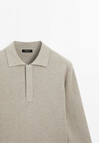 Light beige long-sleeve knit polo shirt with a classic collar and concealed placket, displayed on a white background.
