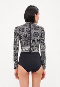 Maillot de bains à manches longues noir et blanc à motifs avec un col montant, un bas noir uni contrastant et un détail de fermeture éclair à l'arrière.
