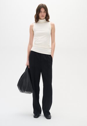 White sleeveless turtleneck top, ribbed texture, paired with black wide-leg trousers. Model carries a large black leather bag.