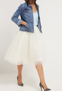 Chaqueta de denim con top azul claro, falda de tul blanca y zapatos de tacón grises. La falda presenta un diseño en capas y aireado.