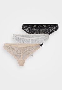Tre par med blondetanga i svart, hvit og nude, med blomsterdesign og bølgekant, i en myk, gjennomsiktig tekstur.