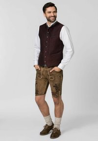 Braune Lederhosen mit floralen Stickereien, kombiniert mit einer burgunderfarbenen Weste und einem weißen Hemd. Braune Schuhe und graue Socken runden das Outfit ab.