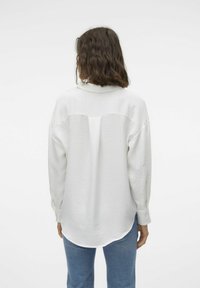 White, textured long-sleeve shirt with a collar, back pleat, and buttoned cuffs, paired with light blue jeans.