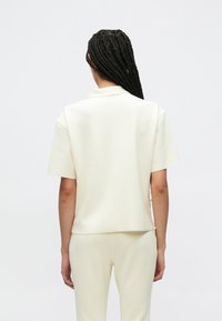 Κρεμ πόλο μπλούζα με κοντά μανίκια, κατασκευασμένη από λείο, ελαφρύ ύφασμα. Διαθέτει κλασικό γιακά και άνετη, τετράγωνη εφαρμογή.