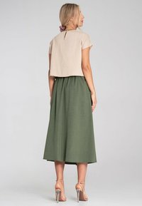 Beżowy krótki top z krótkimi rękawami w połączeniu z długą oliwkową spódnicą. Strój ma detale w postaci otworu na plecach oraz przezroczystą teksturę.