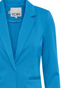 Lys blå skræddersyet blazer med notch-rever, enkelt knaplukning og to klaplommer, størrelse small med ICHI mærke.