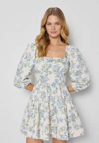 Witte jurk met blauw bloemenpatroon, vierkante halslijn, poffende mouwen, gelaagde rok en een gladde stofstructuur.