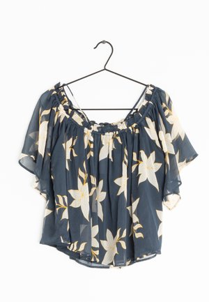 Blouse bleu marine épaules dénudées avec imprimé floral blanc et jaune suspendue sur un cintre fil noir sur fond blanc.