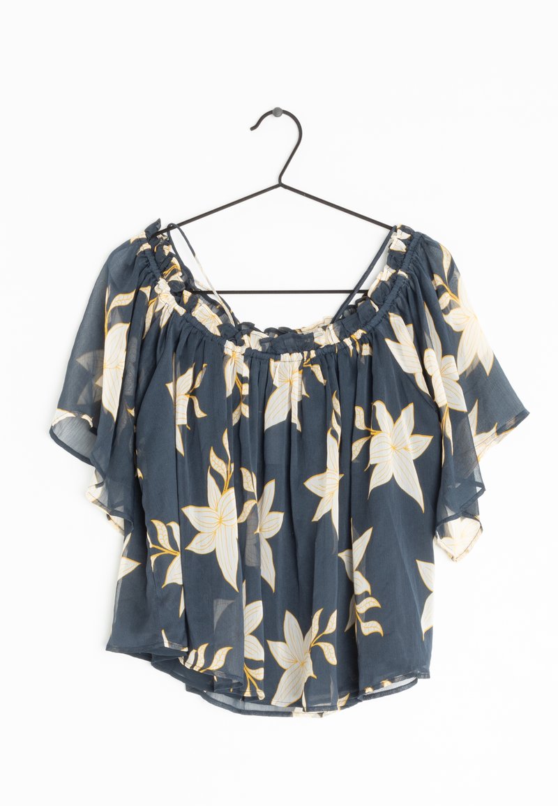 Blouse bleu marine épaules dénudées avec imprimé floral blanc et jaune suspendue sur un cintre fil noir sur fond blanc.