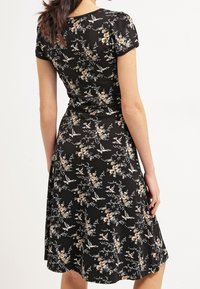 Blommönstrad svart klänning med en figurformad överdel, korta ärmar och en utsvängd kjol. Materialet har en slät textur med fågel- och blommönster.