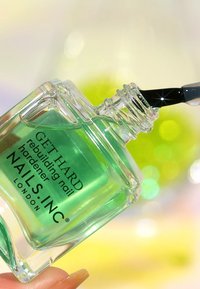 Bottiglia di vetro trasparente di indurente per unghie verde con pennello applicatore nero. Il testo sull'etichetta include "GET HARD" e il nome del marchio "NAILS.INC".