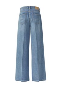 Jean large en denim bleu clair vu de dos avec deux poches arrière et un patch de marque en cuir marron sur la ceinture.