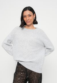 Helehall suurte mõõtmetega kampsun, mis on valmistatud pehmest, tekstuuriga materjalist, laia kaeluse ja soonikkoes varrukasäärtega, kombineeritud mustade litritega pükstega.