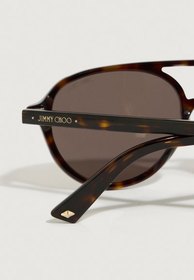 Tortoishell zonnebril met bruin glas, voorzien van gouden "JIMMY CHOO" branding op de scharniers. Inclusief een kenmerkende gouden accent op de arm.