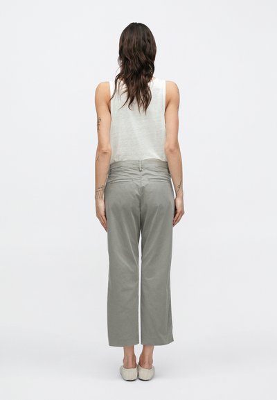 Pantalon gris clair à jambes larges en tissu doux, avec une texture lisse, des poches latérales et un détail à la ceinture arrière. Porté avec un débardeur blanc.