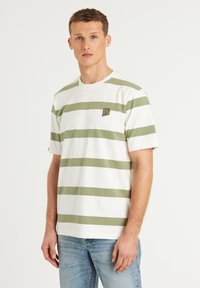 Dryžuota balta ir alyvuogių žalios spalvos marškinėlių, pagamintų iš švelnios medvilnės. Apvalios kaklo iškirptės ir mažas trikampis logotipas ant krūtinės.