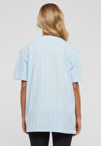 Hellblaues oversized T-Shirt mit weißen vertikalen Streifen, kurzen Ärmeln und rundem Ausschnitt. Weiches Baumwollmaterial, lockere Passform.
