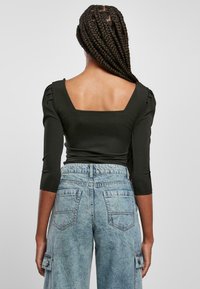 Svart, tettsittende topp med trekvart lange ermer og firkantet rygg. Kombinert med lys blå, høytlivte, slitte denimjeans med cargolomme.
