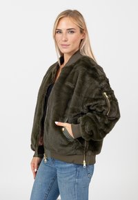 Olivgrüne Kunstfell-Bomberjacke mit gerippten Bündchen und Kragen. Verfügt über Reißverschlusstaschen und ein goldfarbenes Reißverschlussdetail. Weicher Textur.