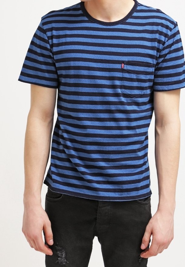 Blå och marinrandig t-shirt i bomull; har rundad hals och en liten bröstficka på vänster sida. Matchas med svarta jeans.