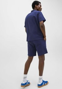 Chemise à manches courtes texturée navy et shorts assortis, associés à des baskets bleues et des chaussettes blanches. Design simple, coupe décontractée.