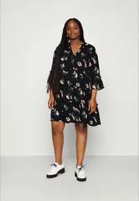 Black floral dress with ruffled sleeves, featuring pink and green flower patterns, a tiered design, and a V-neckline. Worn with white shoes.