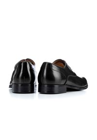 Chaussures habillées en cuir noir avec une finition lisse, bout rond et talon plat. Présentent des coutures discrètes et un design à lacets pour un maintien sécurisé.