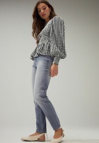 Blusa a cuadros en blanco y negro con mangas abullonadas, cintura peplum, vaqueros de pierna recta en azul claro y zapatos de tacón en beige.