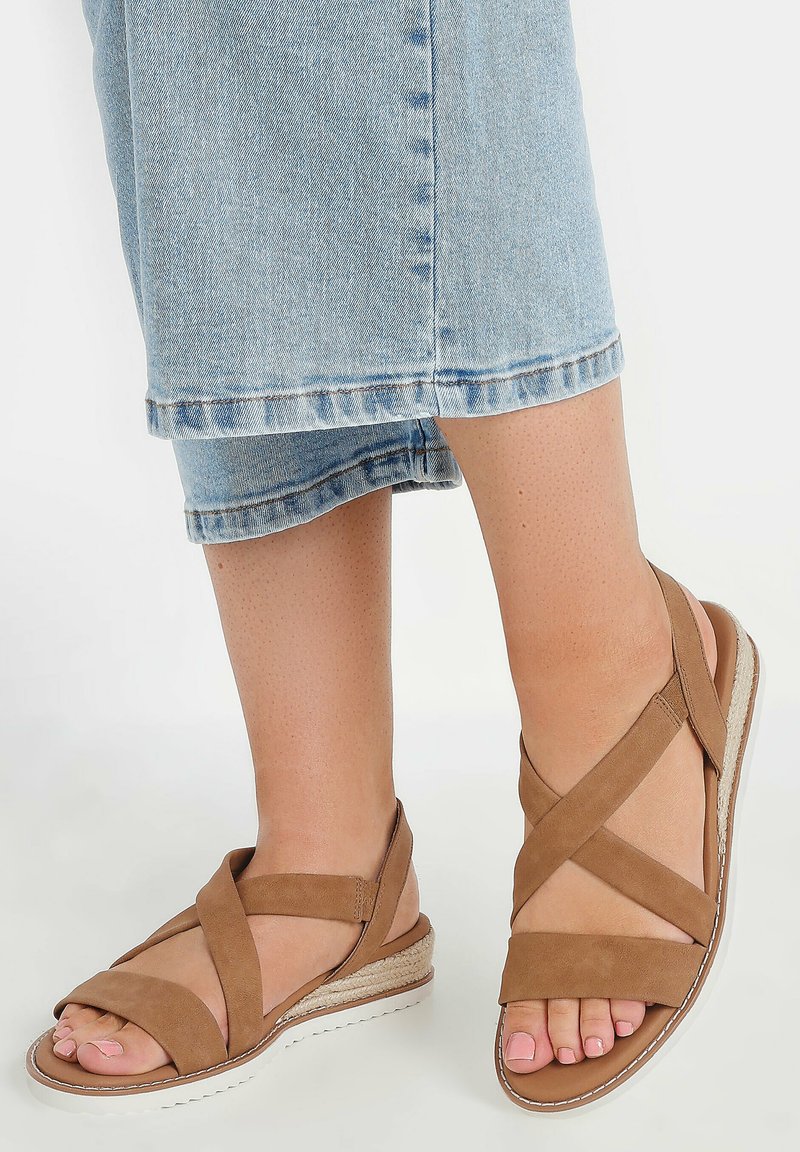 Ruske suede wedgesandaler med krydsende stropper, tekstureret sål og en 2-tommer espadrille-stil hæl. Lyseblå denimjeans, der kigger ovenfor sandalerne.