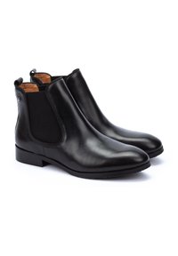 Botas Chelsea de cuero negro con paneles laterales elásticos y costuras mínimas. Punta redondeada y suela plana, con una lengüeta en la parte trasera.