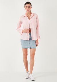 Light pink button-up shirt with long sleeves, single chest pocket, paired with a light blue denim mini skirt and white sneakers.