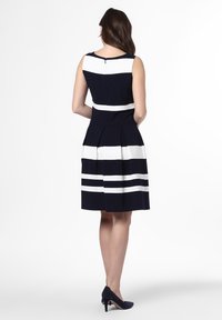 Námořnická modrá šaty s bílými horizontálními pruhy, bez rukávů, s plisovanou sukní a zadním zipem. Dokončeno klasickým, přizpůsobeným siluetou.