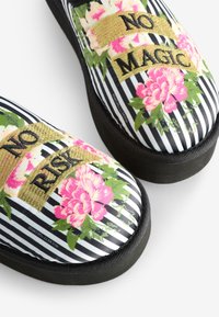 Scarpe da tela a righe bianche e nere con vivaci motivi floreali, ricami dorati con il testo "NO RISK" e "NO MAGIC." Suole nere.